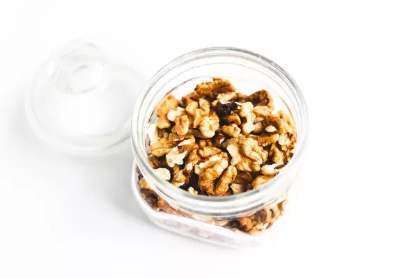 Glass jar of shelled raw walnuts on white background