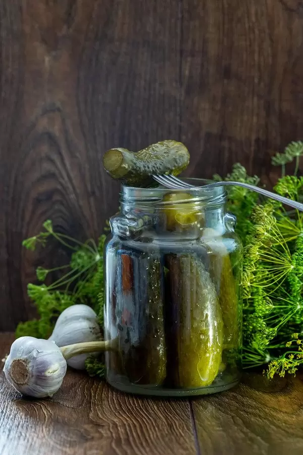 Glass jar with pickles, dill and garlic on wooden background
