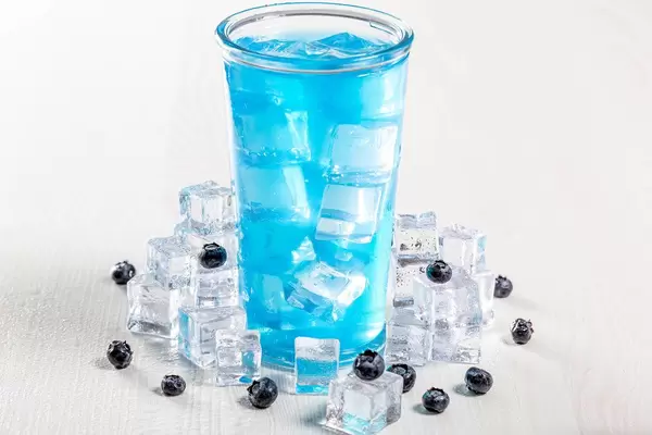 Glass of blue cocktail with ice and fresh blueberries