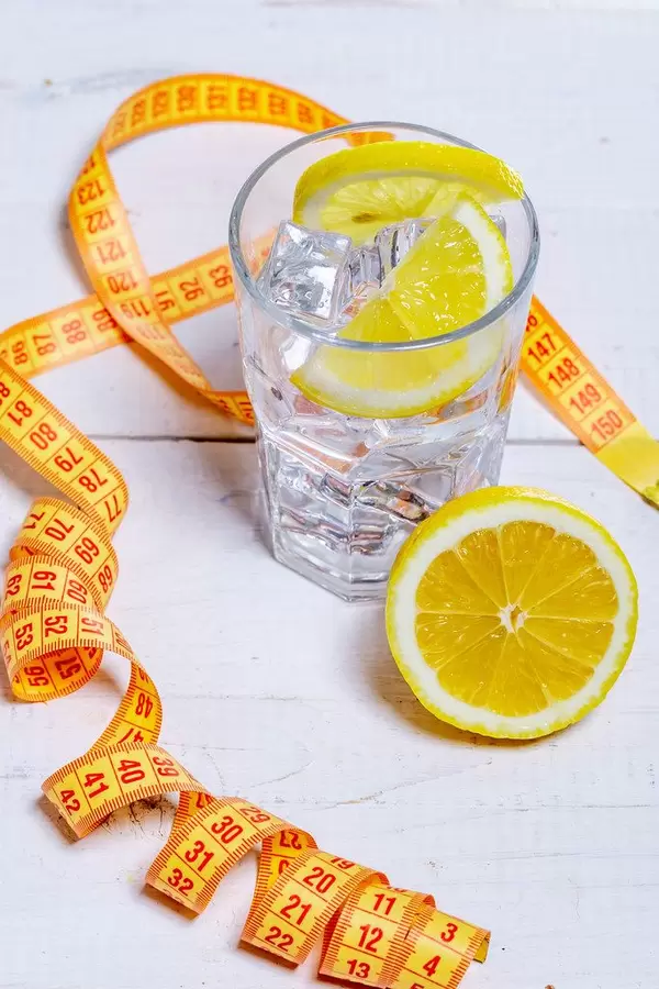 Glass of cold water with ice cubes and lemon on white wooden background with measuring tape-healthy lifestyle concept
