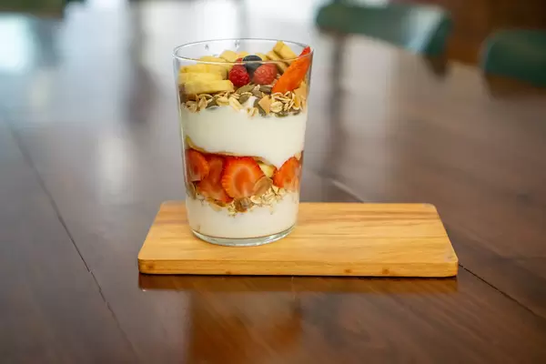 Glass of Mixed Yogurt with Cereals, Banana, Strawberries, Blueberry, Raspberry and Sunflower Seeds on a Wooden Serving Board