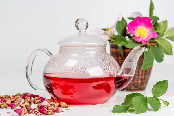 Glass teapot with red tea and tea rose flowers on a white background
