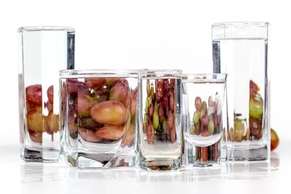 Glasses of different sizes with water and grapes behind them. Distort and display