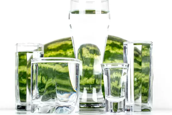 Glasses of different sizes with water with watermelon in the background