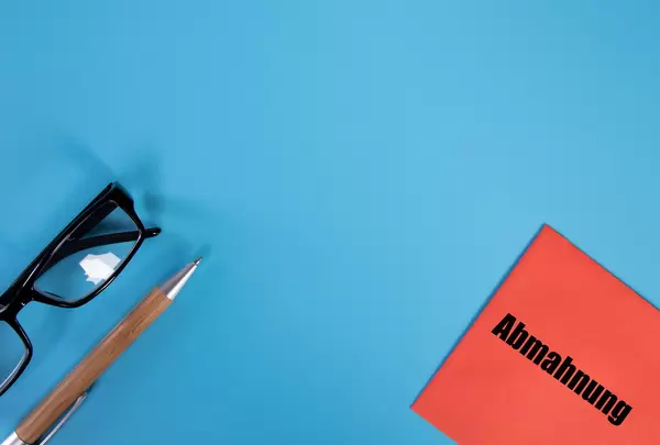 Glasses, pen and red envelope with Abmahnung text on blue background