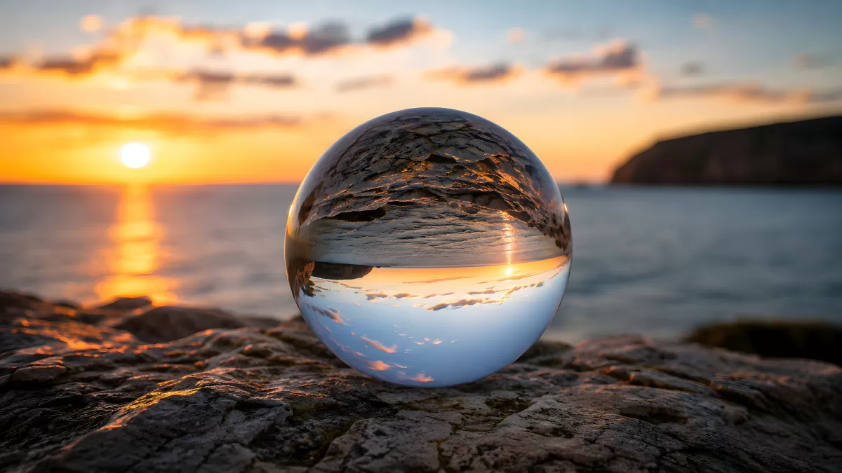 Glasskugel spiegelt Sonnenuntergang am Meer wider