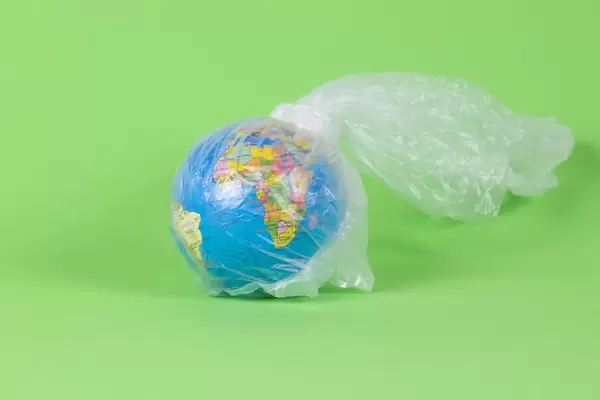 Globe in a plastic bag on green background - Concept on the worldwide plastic problem