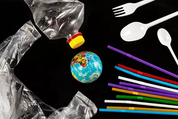 Globe, plastic disposable tableware, bottle and package on black background, planet garbage pollution concept