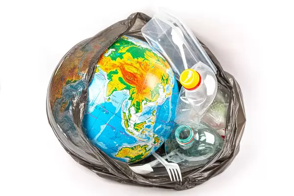 Globe with plastic utensils in black trash bag, planet pollution concept