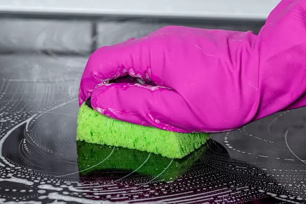 Gloved hand with a washcloth washes a black electric stove