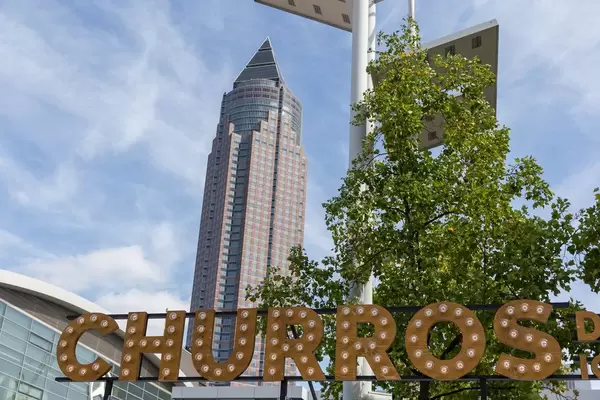 Glühbirne auf Holzbuchstaben des Schriftzugs  "Churros", mit Messeturm Frankfurt im Hintergrund