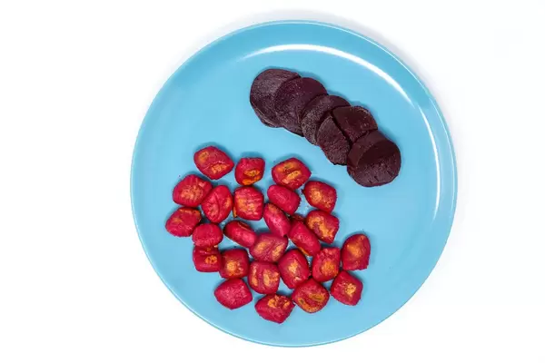 Gnocchi mit roter Beete und Scheiben roter Beete auf einem blauen Teller in der Aufsicht