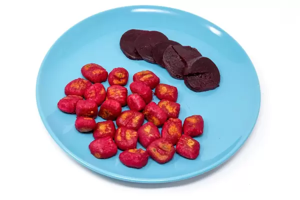 Gnocchi mit roter Beete und Scheiben roter Beete auf einem blauen Teller