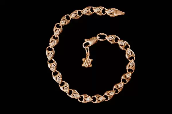 Gold bracelet of hearts with a turtle pendant on a black background