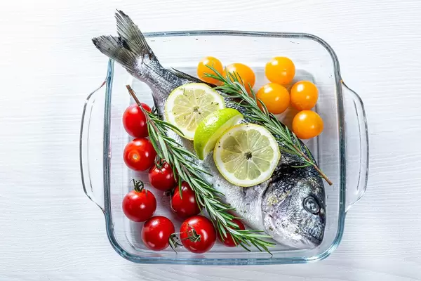 Goldbrasse - Speisefisch, mit Gemüse und Kräutern in einer Auflaufform aus Glas