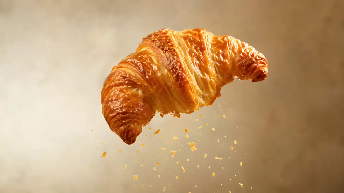 Goldbraunes Croissant schwebt mit fallenden Krümeln — Bild kostenlos herunterladen