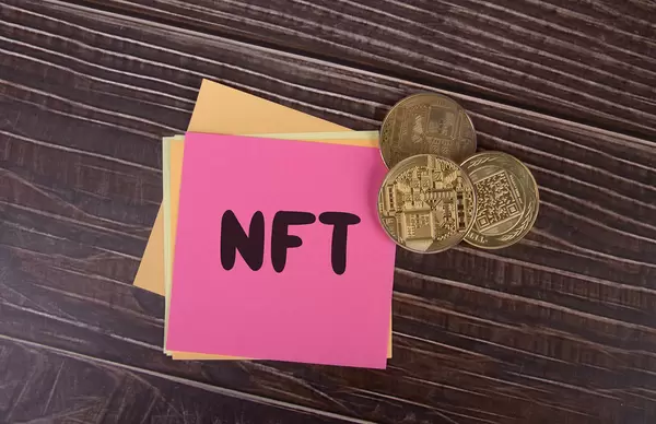 Golden coins and sticky notes with NFT text on wooden table
