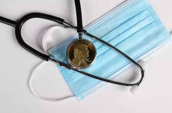 Golden Donald Trump coin with stethoscope and face mask on white background
