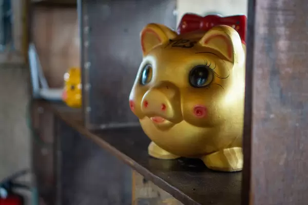 Golden Piggy Bank with Big Eyes and Red Bow Tie in a Wooden Shelf as Decoration in a Restaurant in Vietnam