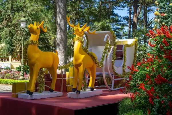 Golden Reindeer with White Sleigh, Christmas Tree and Presents as Christmas Decorations in a Park at Sunny Weather.