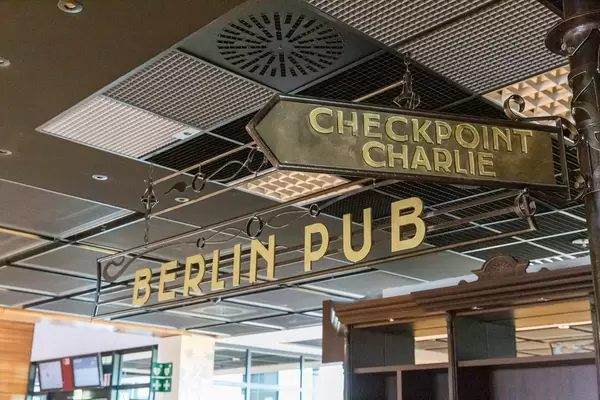 Golden sign of "Berlin Pub" with old style signpost for Checkpoint Charlie at the new BER airport
