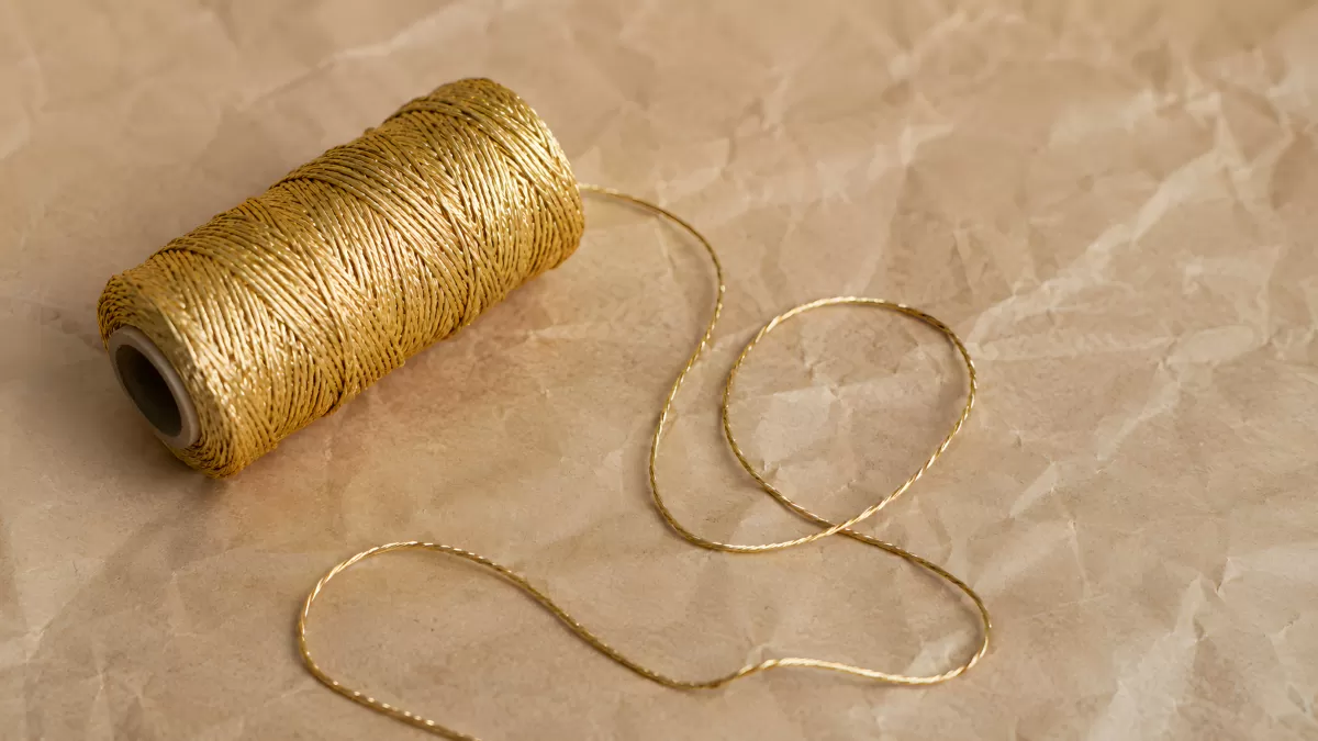 Goldene Garnrolle mit losem Faden auf Packpapier