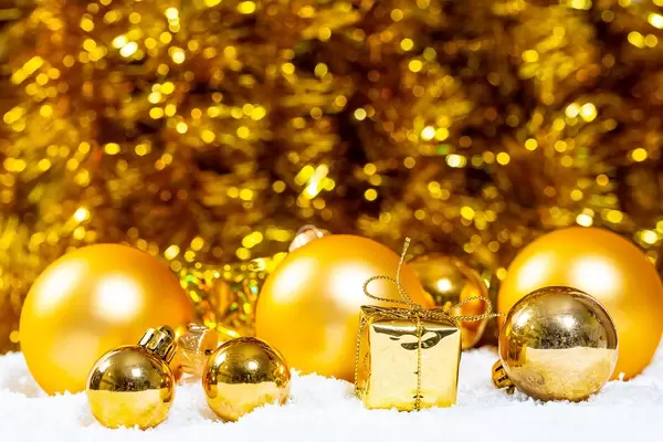 Goldene Weihnachtsbaumkugeln im Schnee vor goldenem Hintergrund