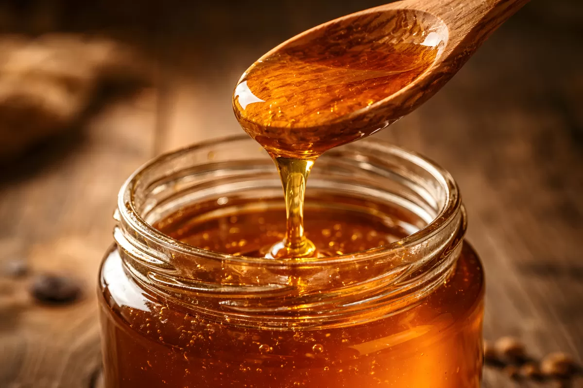 Goldener Honig fließt vom Holzlöffel ins Glas