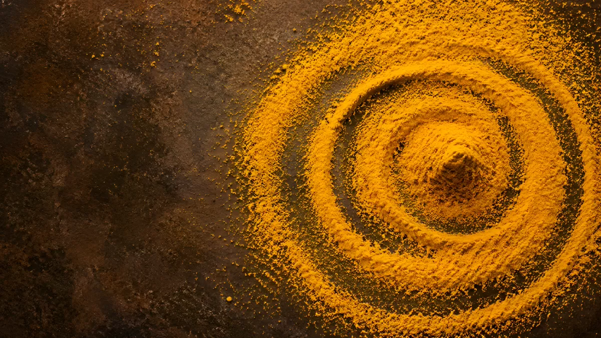 Goldgelbes Kurkuma-Pulver in Spiralform auf dunklem Stein