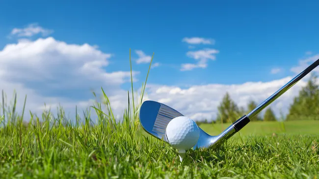 Golfball auf Abschlag mit Golfschläger bei Sonnenschein