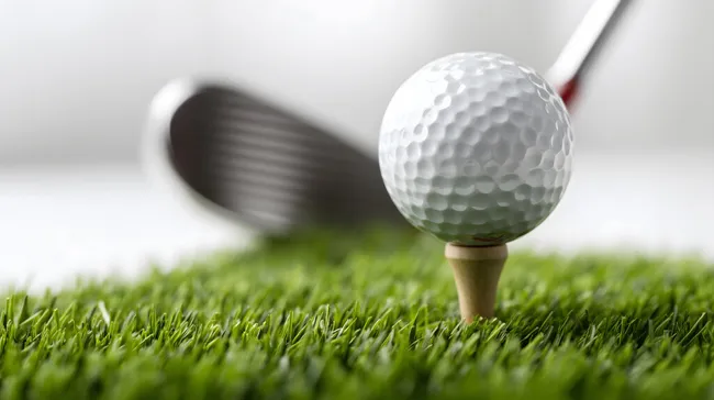 Golfball auf Holztee im grünen Gras