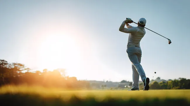 Golfer beim Abschlag auf sonniger Golfplatzkulisse