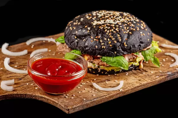Gourmet black burger with spicy sauce on wooden board