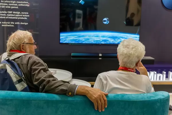 Grandparents rest on the couch during the high-tech exhibition IFA in Germany, with 75 8K Mini LED television in the background