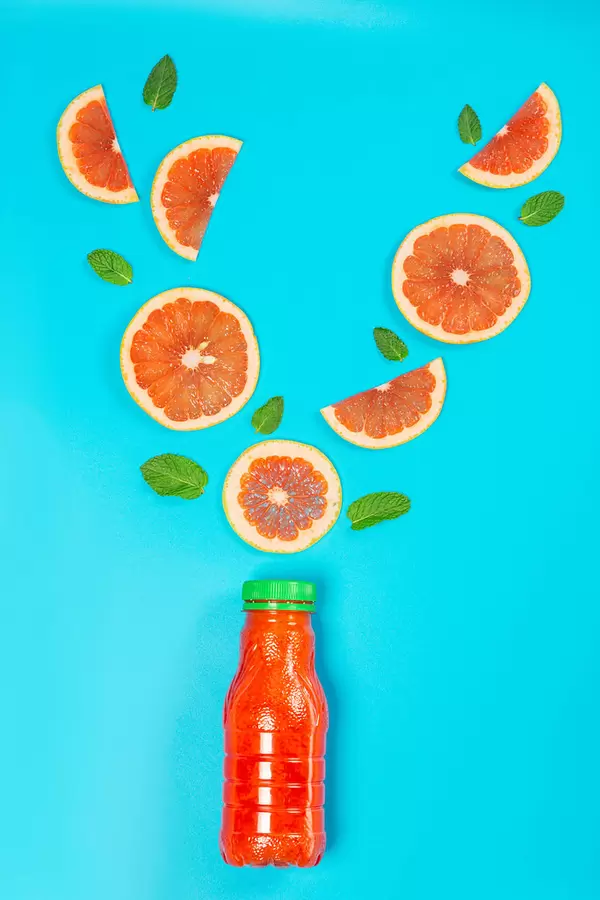 Grapefruit juice bottle with grapefruit pieces and fresh mint leaves on blue background