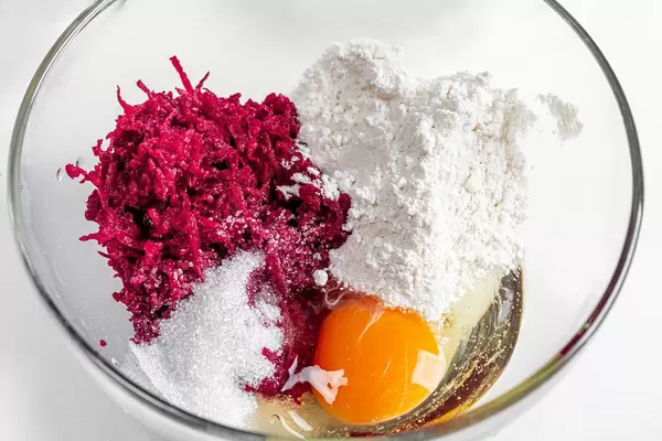 Grated beetroot, flour, sugar, soda and egg in a glass bowl close-up