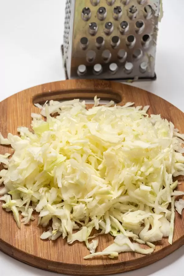 Grated cabbage salad on the round wooden board with metal grater
