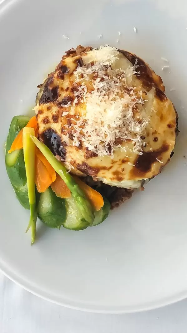 Greek dish Moussaka made of minced meat, cheese and green asparagus on a white plate