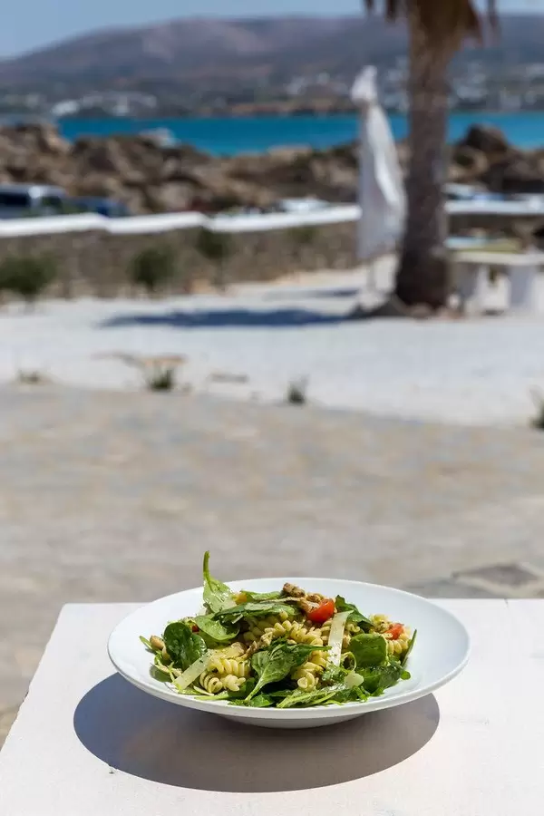 Greek noodle dish with green leaves, tomatoes and parmesan cheese on an outside table near the beach