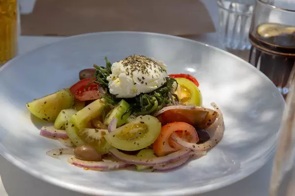 Greek salad with green tomatoes, onions and olives on a white plate in a Restaurant in Greece