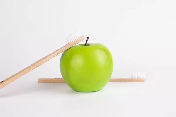 Green apple with wooden toothbrushes on white background