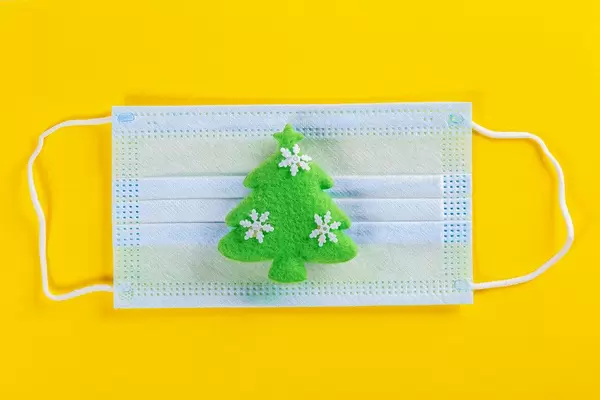 Green christmas tree toy with medical mask on yellow background