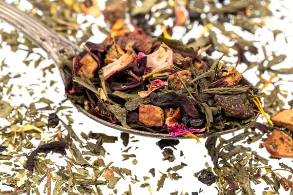 Green dry tea with dried fruits and petals in a spoon