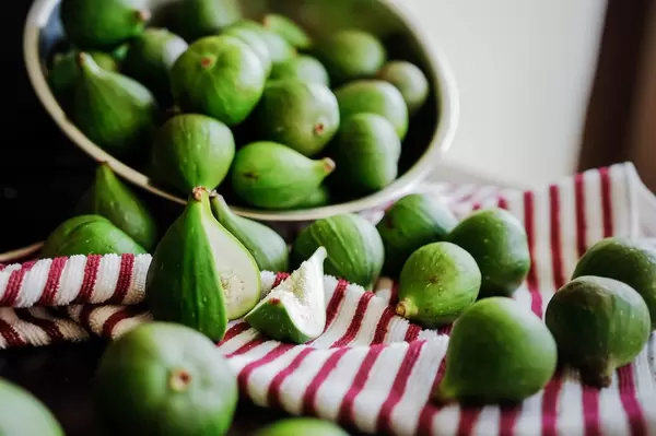Green figs coming out of a metal bowl to a kitchen cloth