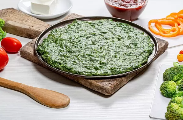 Green pizza base and fresh vegetables on white table