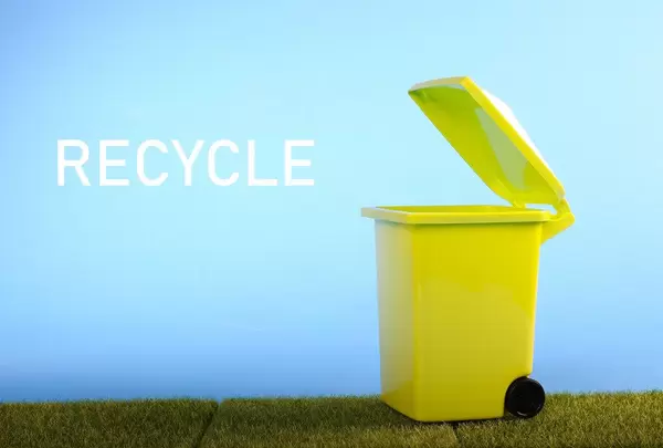 Green recycle bin on green grass and blue sky