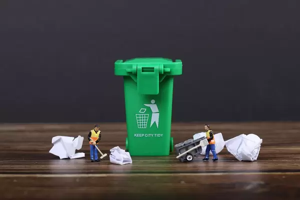 Green recycle bin with screwed up paper and tiny  cleaning workers