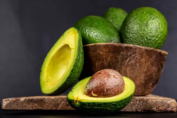 Green ripe avocado in a wooden bowl on a dark background