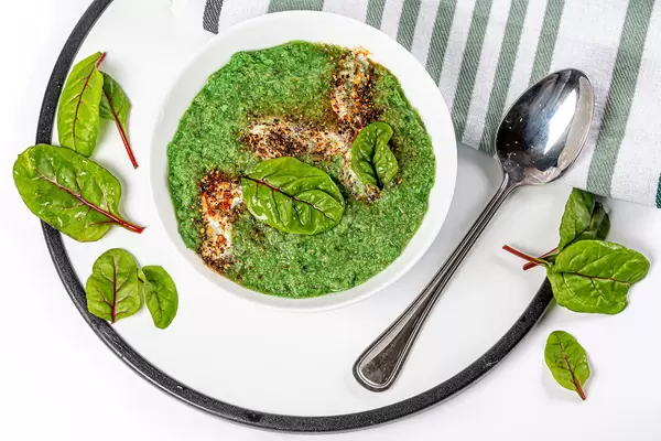 Green soup puree in a white bowl with mangold leaves and spoon, top view