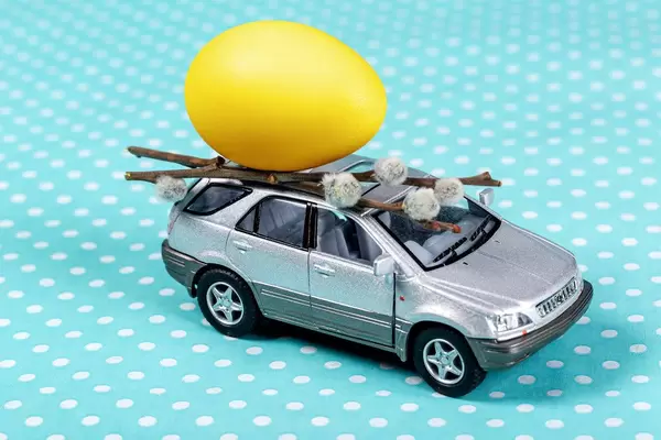 Grey toy car with a yellow egg and willow branches on a blue background